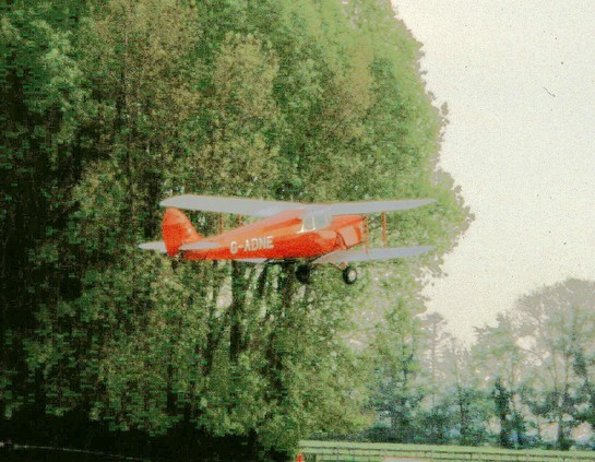 Red and silver cabin biplane taking off, pictured against a stand of trees.