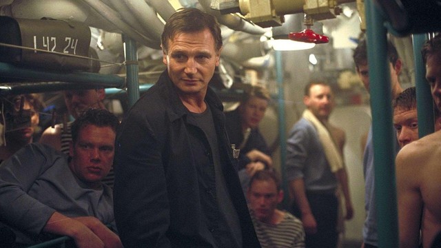 Liam Neeson steht zwischen seiner Besatzung in den Gängen eines Ubots und schaut schelmisch drein.