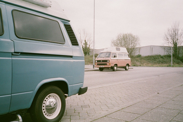 half of a blue van. in the background is another van which is white & brown