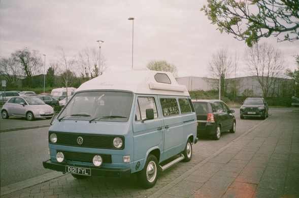a blue volkswagen camper van. it has shiny hub caps and four lights on the front.