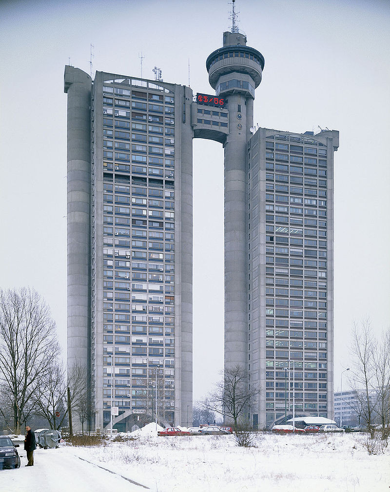 a photo, taken during winter, snow on the ground, there are two towers connects at the top with a bridge between them, above it is a circular unit, it looks like a building from star wars , there is a large digital clock above the bridge, the building is grey colored