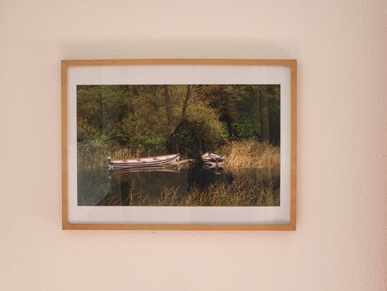 This image depicts a picturesque scene of boats on a serene lake. The composition includes a dominant foreground of brown boats set against a clear, white background. The color palette is accentuated by an earthy tone. The image features a large picture frame in the center, surrounded by a variety of elements such as walls, paintings, art pieces, plants, photographic paper, and grass. The overall composition exudes a sense of tranquility and outdoor beauty. The scene is reminiscent of a peacefu…