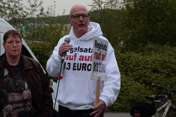 Der Frührentner und Bürgergeldempfänger Thomas Wasilewski trägt Pulli und Schild mit dem Text "Regelsatz rauf auf 813€". 