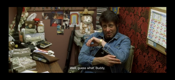 Image from “Kill Bill” showing the image of the owner of the strip club, a masc presenting persons with light skin and dark hair sitting behind desk and wearing a denim jacket
Caption:
“Well guess what Buddy” *pointing at elbow*