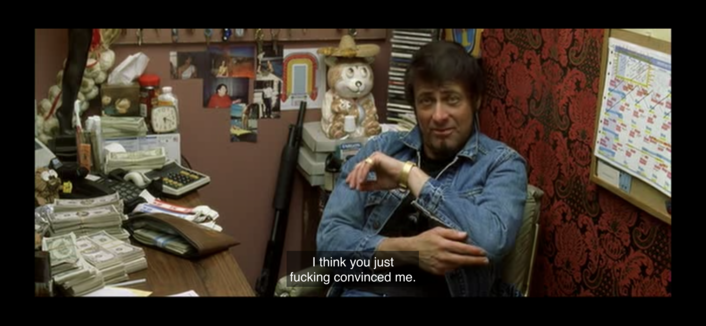 Image from “Kill Bill” showing the image of the owner of the strip club, a masc presenting persons with light skin and dark hair sitting behind desk and wearing a denim jacket
Caption:
“I think you just fucking convinced me.”
 *pointing at elbow*