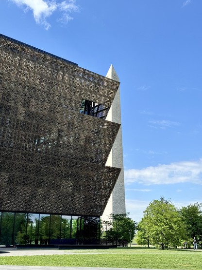 The diagonal lines of the African American Museum cut triangles from the Washington monument behind it