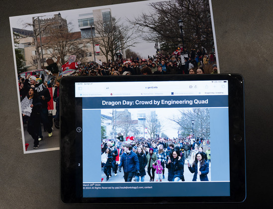iPad tablet with screen reading "Dragon Day: Crowd by Engineering Quad" with the same picture on it as a print behind the tablet that shows a crowd massed on a road.