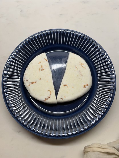A circular piece of homemade paneer sliced in two halves on a blue decorative plate.