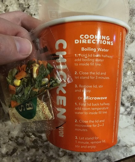 A cup of ramen noodles and the flavor packets that came in it, showing the  instructions that do not even mention what the packets are for