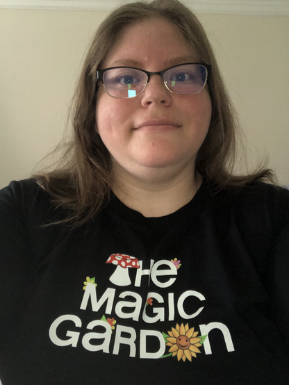 Picture of me wearing a shirt that has the text: The Magic Garden. The T in the is a mushroom and the e in garden is a sunflower with a smiley face on it.