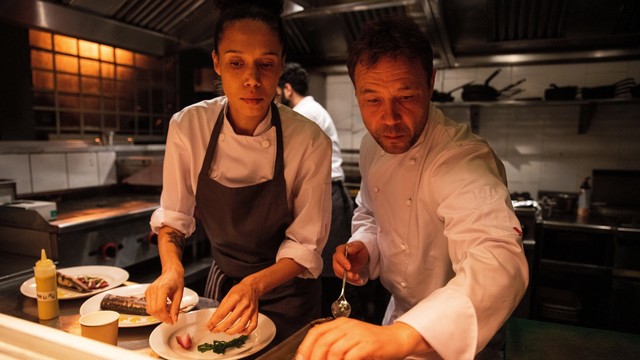 Vinette Robinson und Stephen Graham stehen in kompletten Küchenmontur vor ein paar Tellern und richten diese hochkonzentriert an.