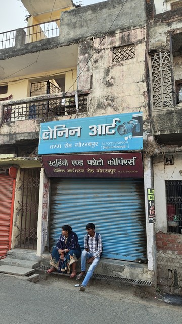 A blue billboard on top of a building which says 'Lenin Art' along with the artists Phone number in India.
