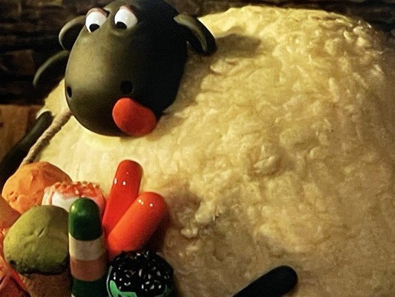 A close-up of a claymation sheep with an assortment of colorful clay objects -ice popsicles- in front of it.