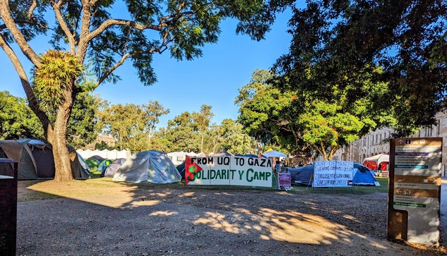 Campus encampment.
University building to the right. 
Trees to the left.
Tents, banners, signs. 
Signs include
"From UQ to Gaza solidarity camp" and "divest from genocide"