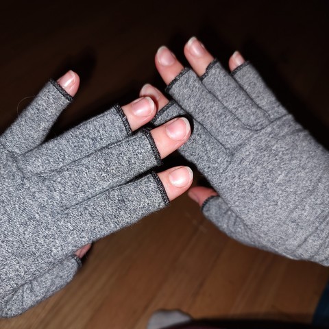 Photo of the hands of a middle-aged white woman wearing gray compression gloves. The gloves have no fingertips.
