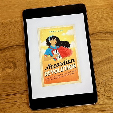 E-book reader with the book cover of my Accordion Revolution. Graphic shows a woman based on the Rosie the riveter propaganda poster from World War II playing a red piano accordion.