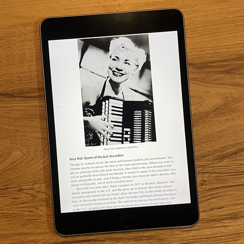E-book reader with a page from my Accordion Revolution book showing Jazz accordionist Alice Hall and text telling her story. Page features a 1940s glamour shot of her smiling and holding her unusual accordion that has what looks like a piano keyboard with three layers, that was really a button accordion disguised as piano Keys.