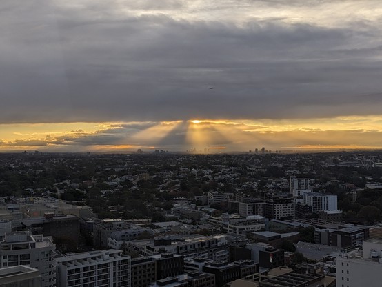 An aerial photo looking west over Sydney, with cloudy heavens parting and beams of golden triangular light streaking down over the distant high-rises of Parramatta. You can't see it in the photo, but there are probably choirs of angels singing.