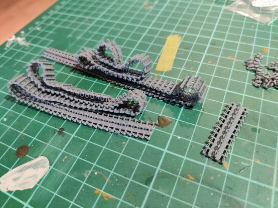 Two caterpillar tracks and a lenght of track armour for a 1:35 scale Panzer IV mode, lying side by sidel. These fully articulated and unpainted 3d-printed resin tracks are loopable and posable.