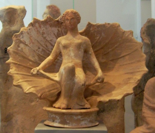 Terracotta figurine of Aphrodite sitting naked in an opening sea shell.