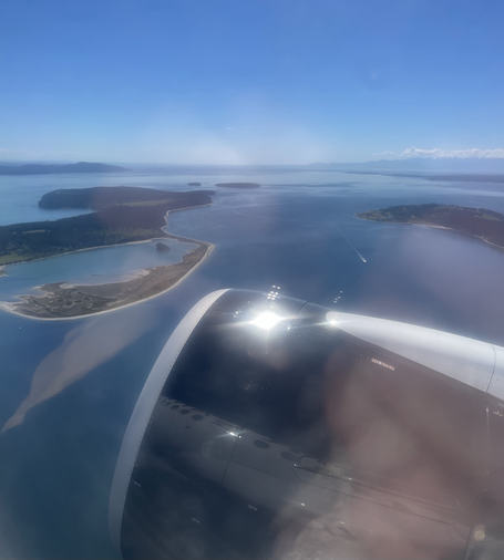 View from an airplane window looking over small islands on a sunny day with blue sky and white clouds on the horizon 