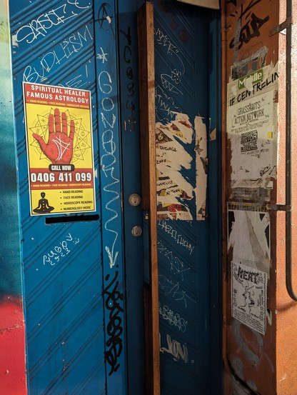 Street doorway.
blue door.
Yellow ad for palmistry.
Several paper flyposters, mostly torn