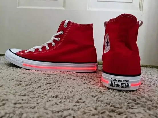 A pair of red converse all star high top shoes with red electroluminescent wire embedded around the sides and heel of the sole.