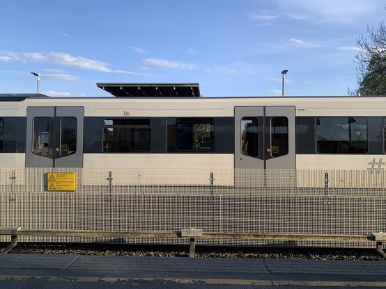 I forgrunnen et skilt hvor det står "hold avstand til plattformkant" I bagrunnen, sporveiens hvite metro-togsett. t-banen ved Berg stasjon.