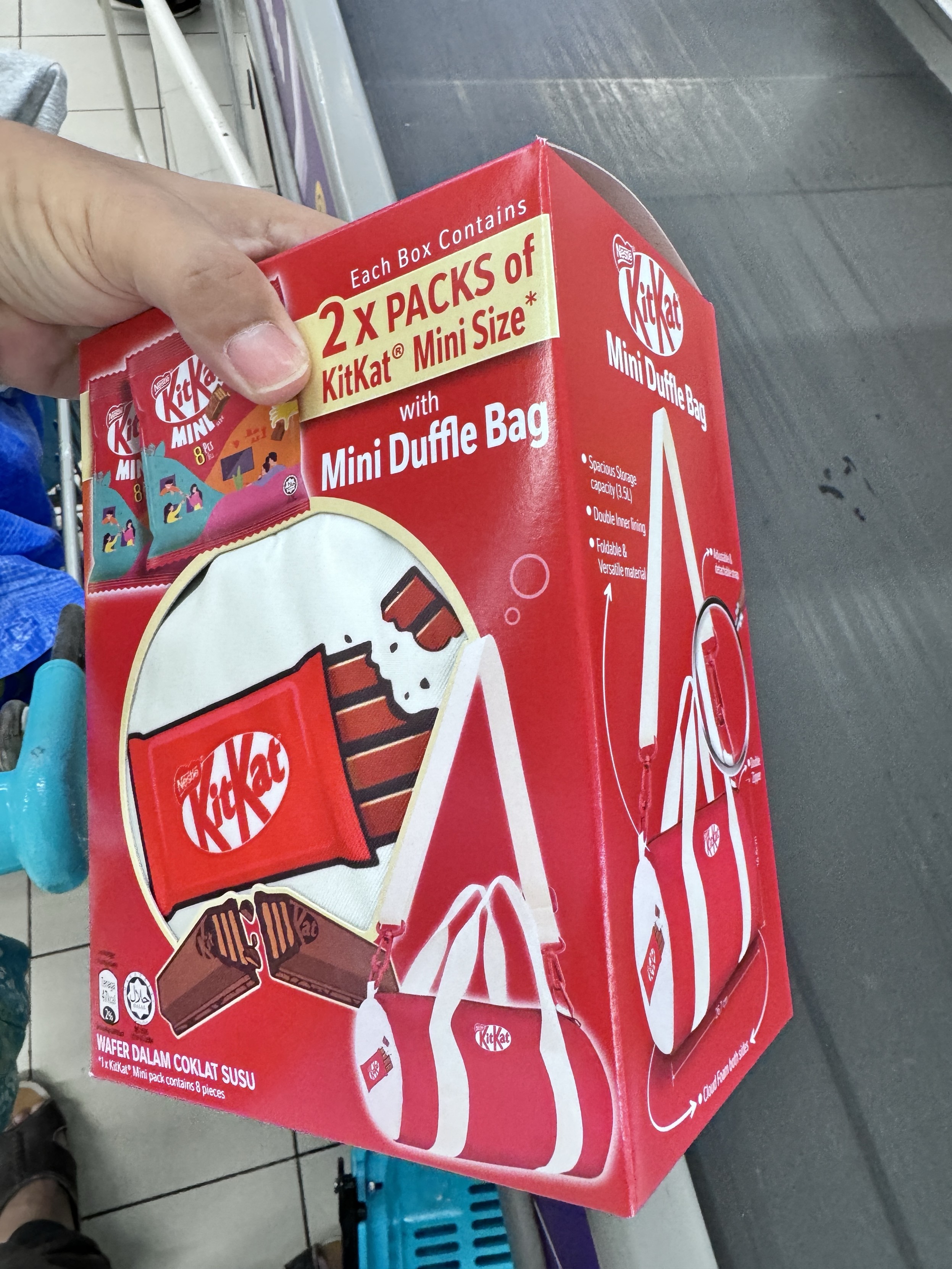 A hand holding a promotional KitKat box that contains two packs of mini-sized KitKats and a mini duffle bag.