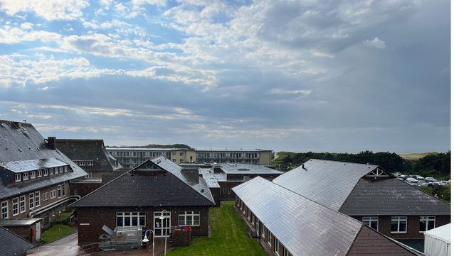 Blick aus dem Fenster im 3. Stock auf Gebäude der Asklepios Reha-Klinik auf Westerland mit einem links blau durchsetzten, rechts eher wolkigen Himmel.