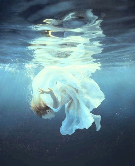 Woman in silence under water with flowing white shear dress