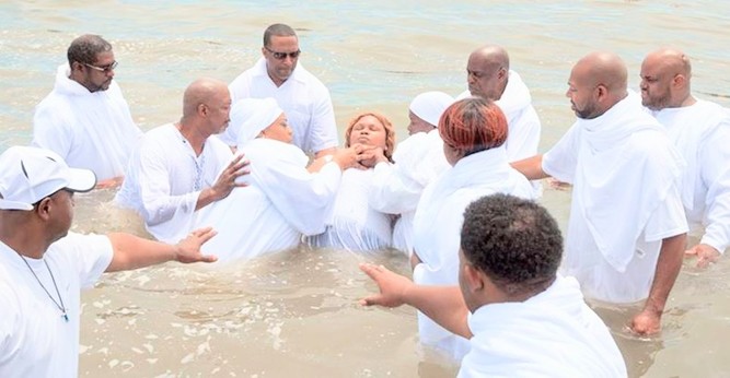 Many people dressed in white standing in water doing baptising