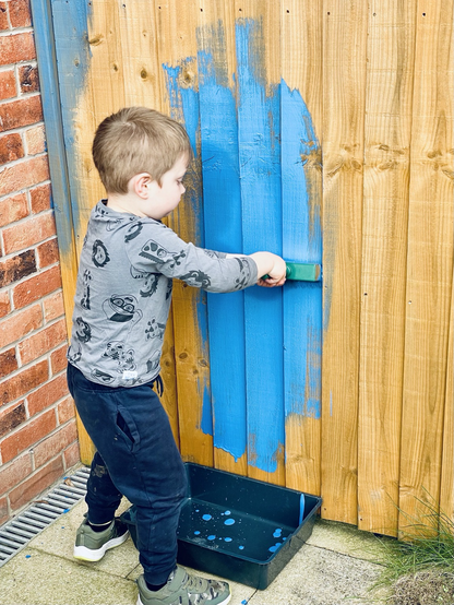 A young boy starting to paint a brown fence blue.