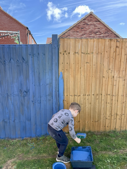 One fence painted blue, another being painted by a young boy.
