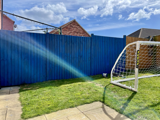 Three fences painted bright blue. A child’s football goal is on the grass.