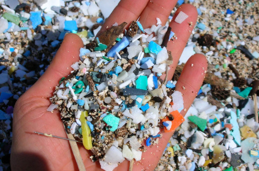 close-up photo of a left hand with the palm holding a pile of small plastic particles. The background underneath is also full of such particles. 
