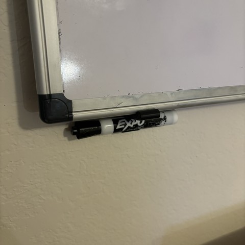 A whiteboard resting on a 3d printed wall hook, with a marker snapped below