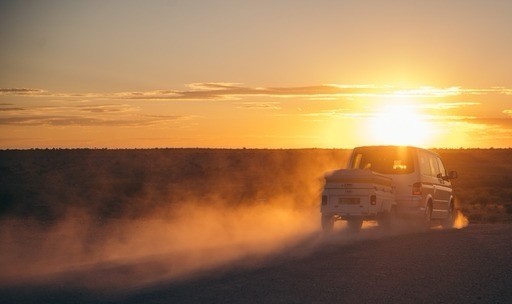 Vehicle driving on a dusty road at sunset.