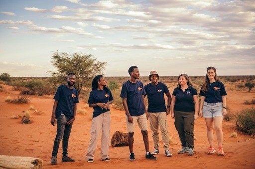 Group of six people in matching shirts standing in a desert landscape.