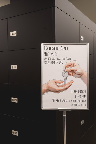 Im Hintergrund sind Bücherschließfächer zu sehen. Davor ein Aufsteller mit dem Hinweis wo man die Schlüssel dafür erhält.