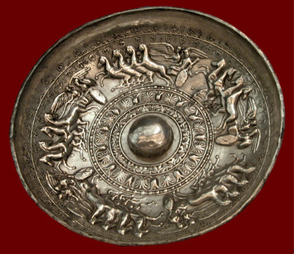 Silver libation bowl with low-relief of chariots with Ares, Athena, Herakles and Dionysos. The libation bowl (phiale) has a round boss in the center surrounded by beautiful repoussé decoration of lotus and acanthus and chariots driven by winged Victories. Each of the four-horsed chariots has a divine passenger with their attributes. Herakles has his club, Ares is in full armour.