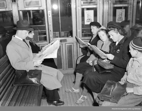 Svart hvit foto av passasjerer som sitter på en trikk. Passasjerene leser i aviser.