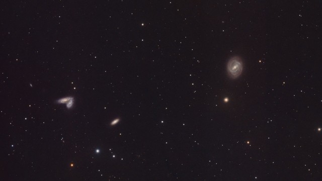 Messier 58 Galaxy (NGC4579):
Black background with many stars of varying brightness spread throughout. 

Upper right of center is the M58 barred spiral galaxy with blue arms and orange glow. At center is a bar with a bright white center.

At lower left are two smaller oblong spiral galaxies that are touching at their tips - one angled away from the other.

There are some other, smaller still, galaxies in the image as well.