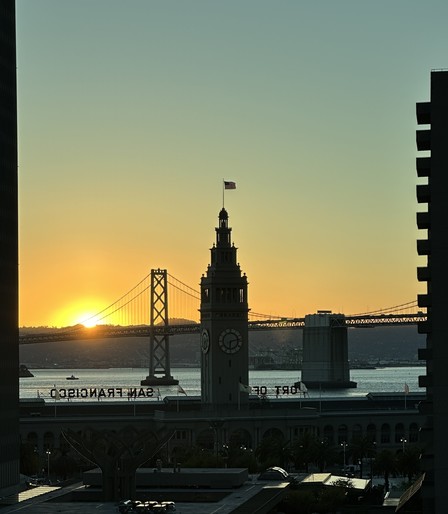 View of sunrise over the bay from the San Francisco financial district. Photo had the Ferry building clock tower and Bay Bridge in the foreground.