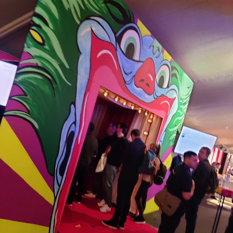 The entrance of speaker room 8, looking like the entrance of a fun ride or haunted house ride. The entrance is the mouth of a clown face with green hair and blue skin.