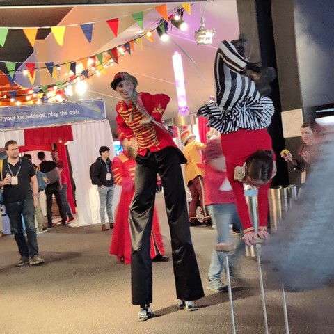 Acrobats and jugglers spicing things up inside the venue. The ceiling is decorated with a garland of colored flags.