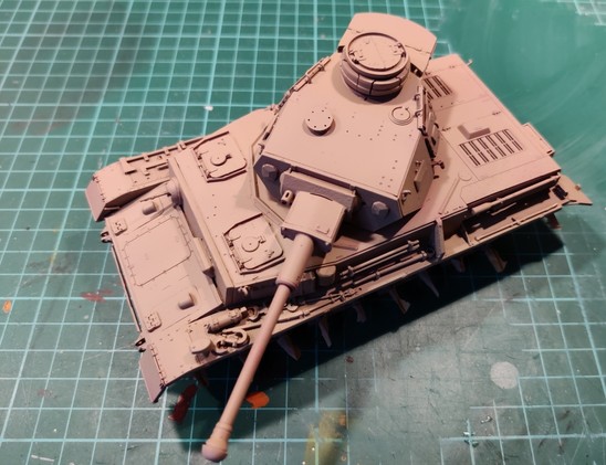 A sandy yellow -painted 1:35 scale model of a Panzer IV without its tracks, on a mistreated hobby mat