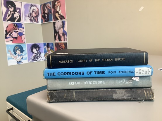Four books stacked horizontally: Agent of the Terran Empire, The Corridors of Time, Operation Chaos, and (obscured) The Trouble Twisters.  In the background there is a rectangle made of anime character squares crossing the corner of two walls.