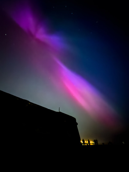 Blue and purple aurora over an old fort with people watching.