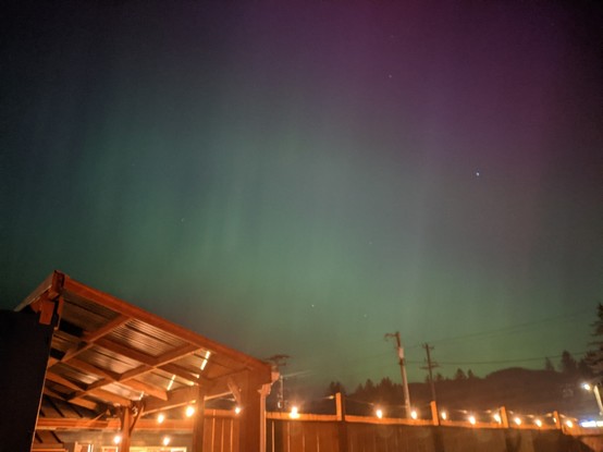 The night sky lit up in particularly fetching shades of green and fuschia. The bottom of the picture is a wooden fence and roof structure strung with small light bulbs. It was pretty damn cool, no lie.